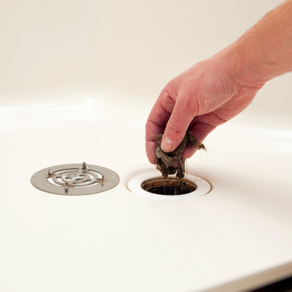 A plumber is removing a clump of hair and debris which has clogged a house shower drain